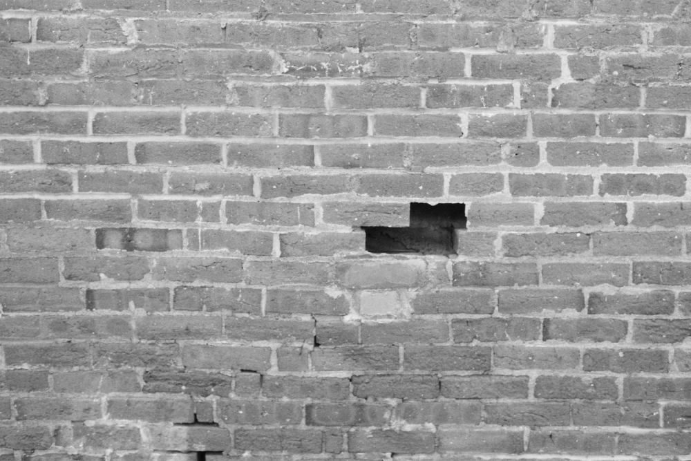 Image: a black and white photo of a brick wall from which two bricks, one immediately above the other, are missing, creating a negative space.