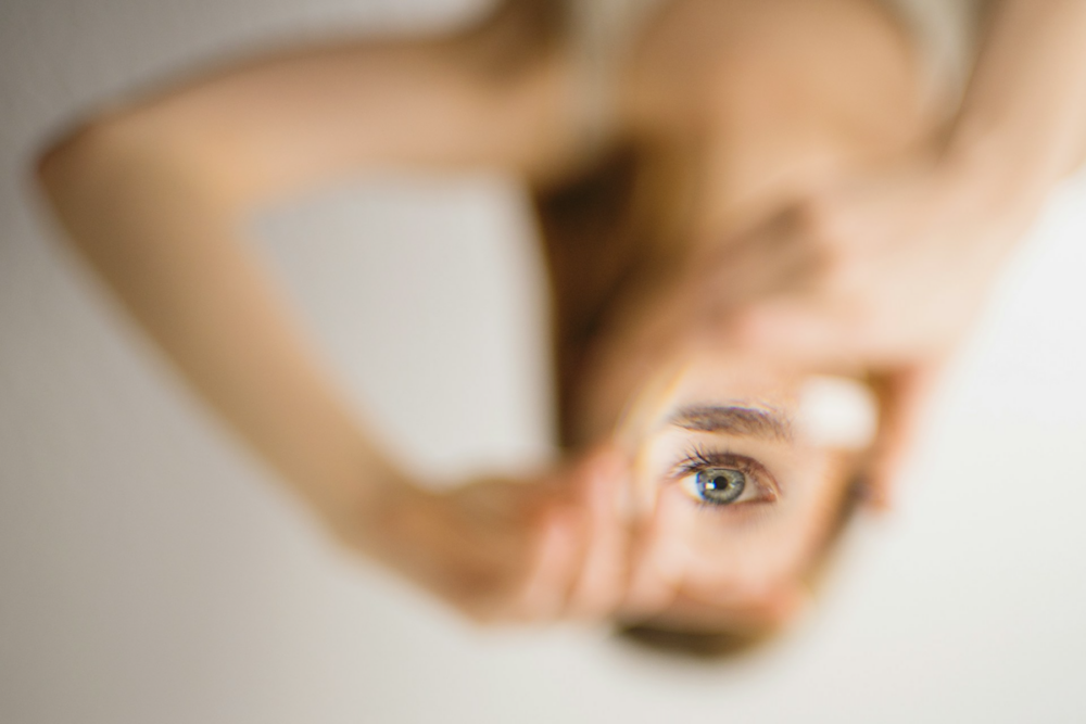 Image: a woman's eye is clearly visible through a lens she's holding, but the rest of her is out of focus.