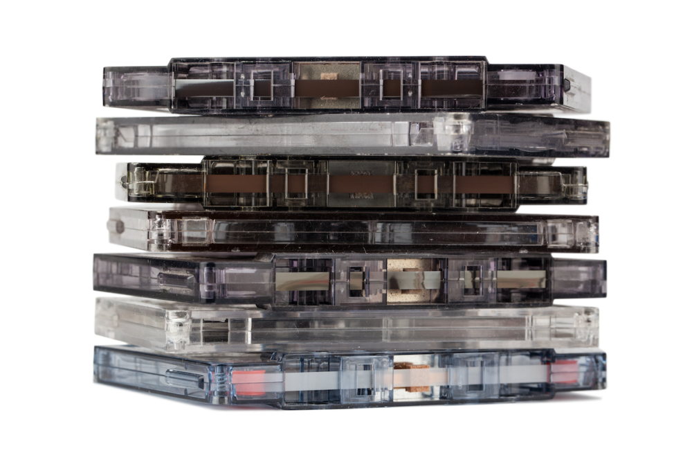 Image: a stack of seven unlabeled cassette tapes.